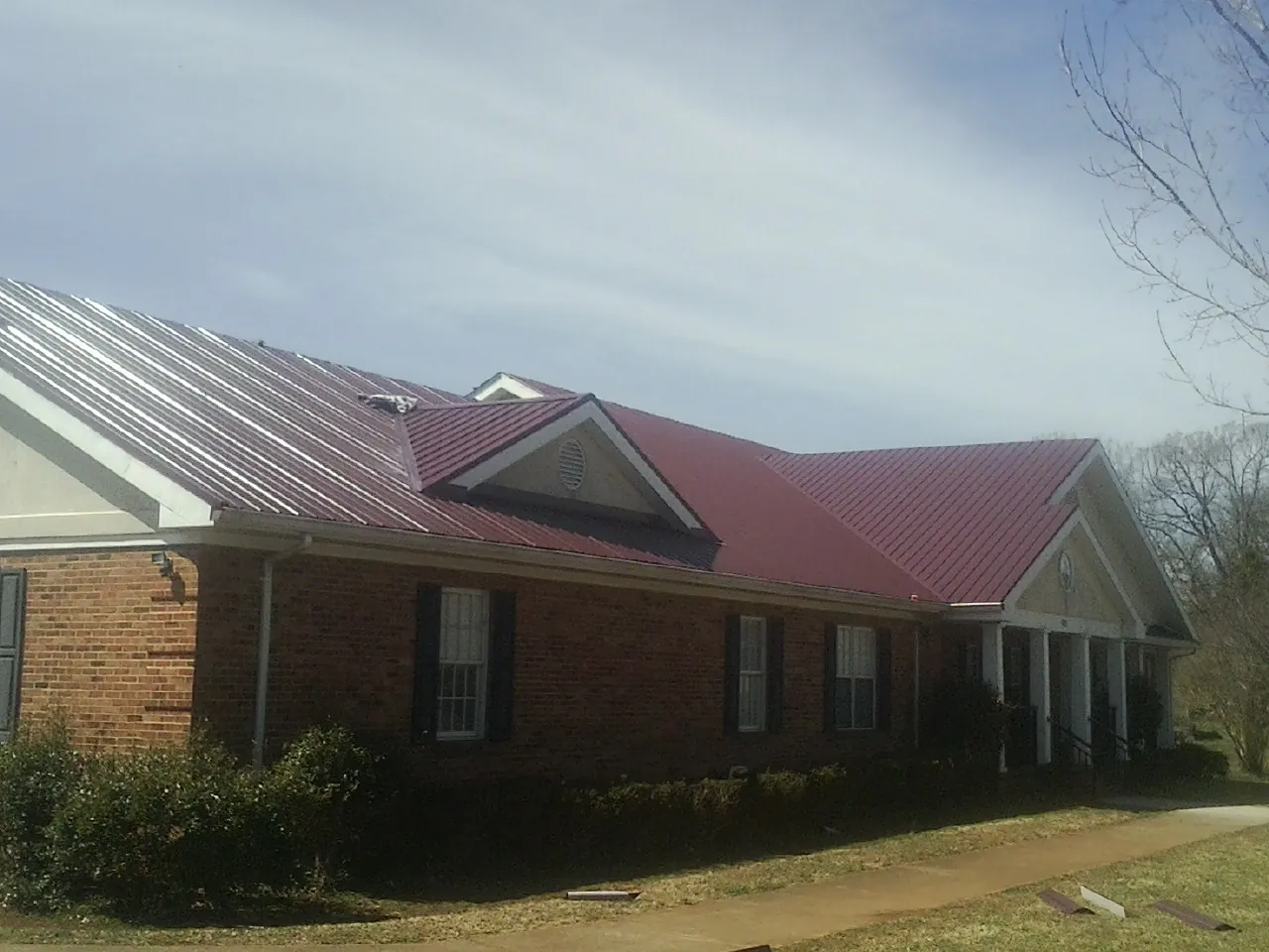Red metal roof with gabled entries on a long brick building, from a Hail Damage Roof Repair job in Bloomingdale