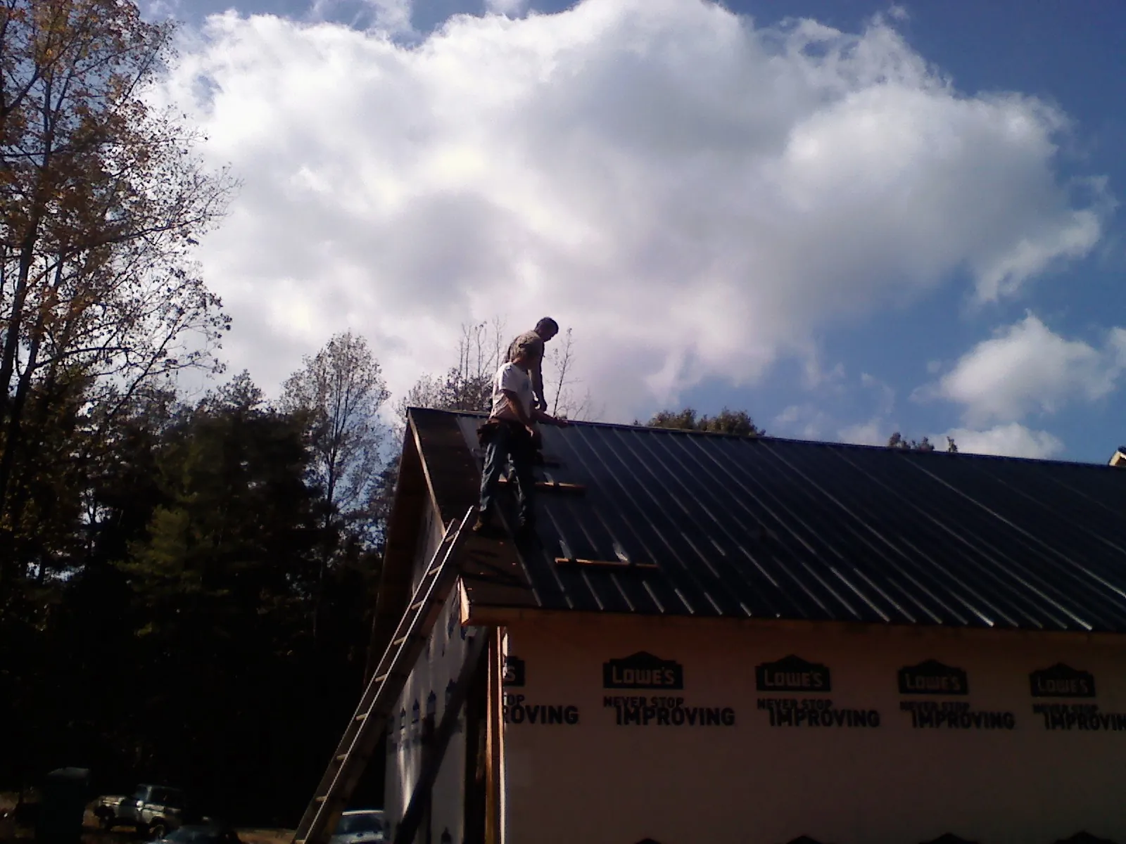 Roofer fastening dark metal panels high against a cloudy sky, from a Roof Inspection job in Bloomingdale